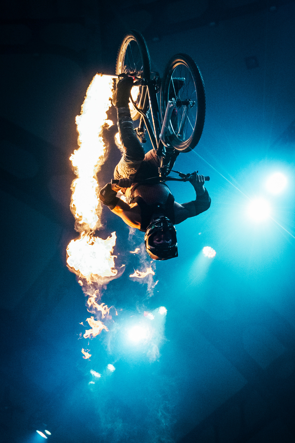 Ruso Bros freeride mountain biker performing a backflip through fire under stage lights